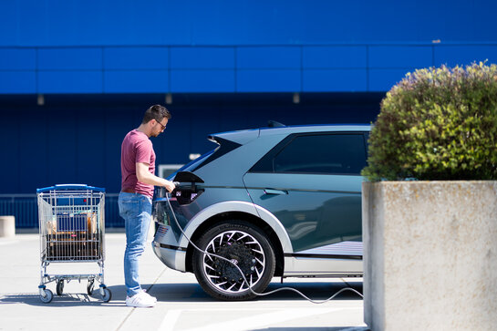 Man laad wagen via laadpaal op de parking van een winkel.