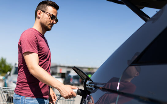 Man plugt laadkabel in elektrische wagen op de parking van een supermarkt