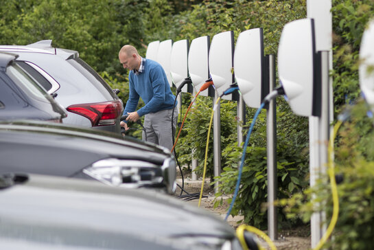 Man plugt laadkabel in elektrische wagen op de parking van het werk